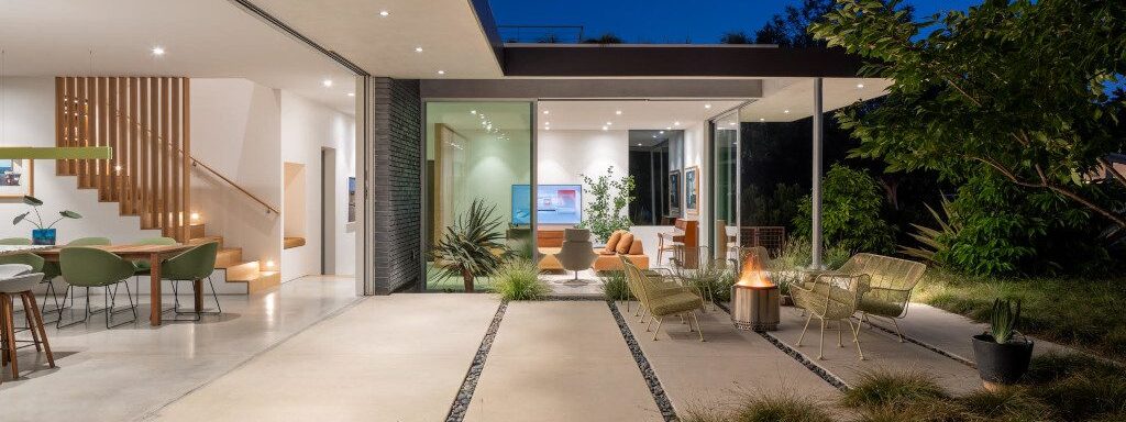 A house open to its courtyard at dusk, lit from inside and out.